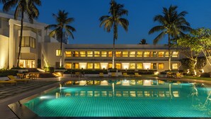 A hotel with a swimming pool, palm trees, and a well-lit exterior. - Trident, Bhubaneswar (Bhubaneshwar)