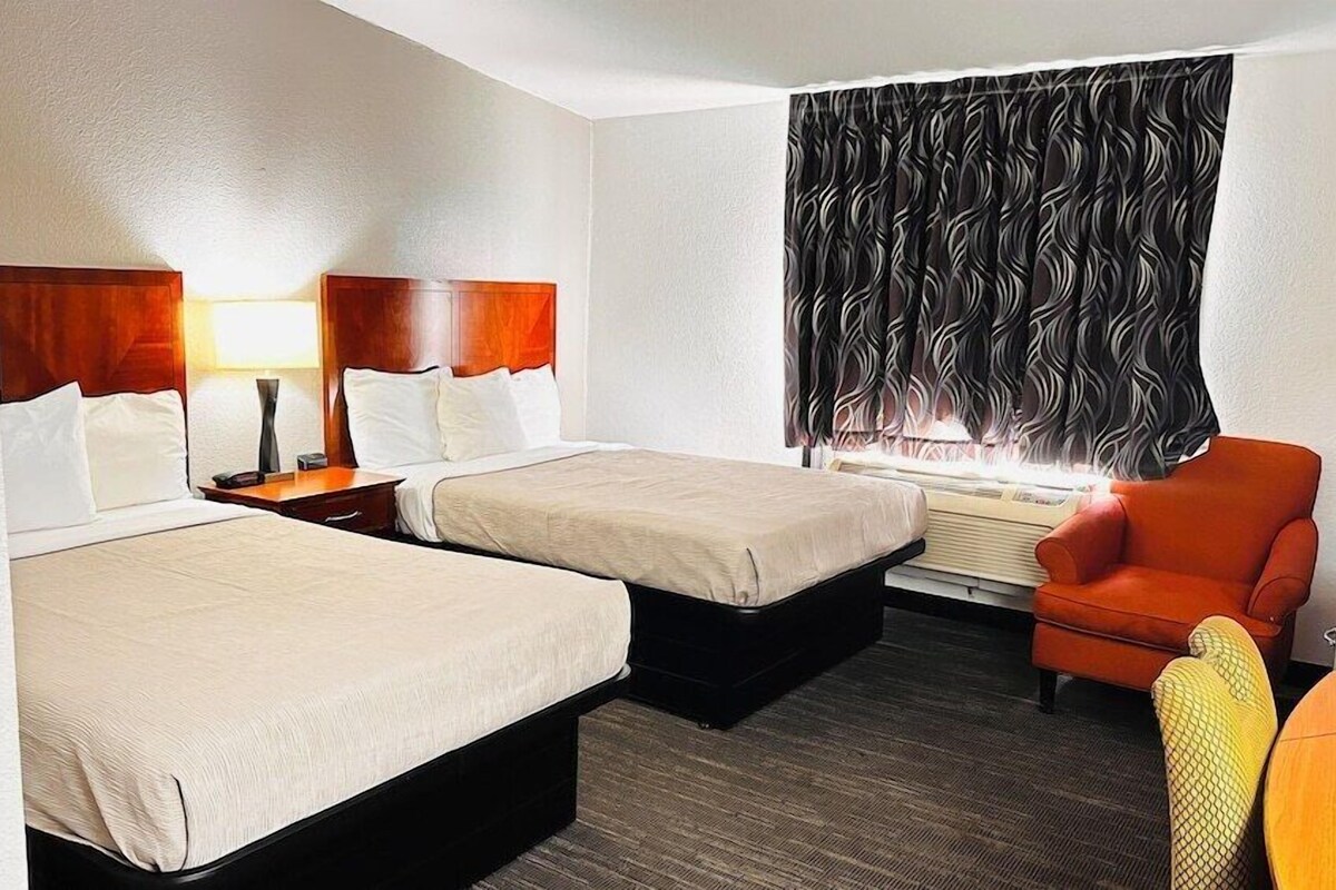 A hotel room with two beds, a desk, a chair, and a window with curtains.