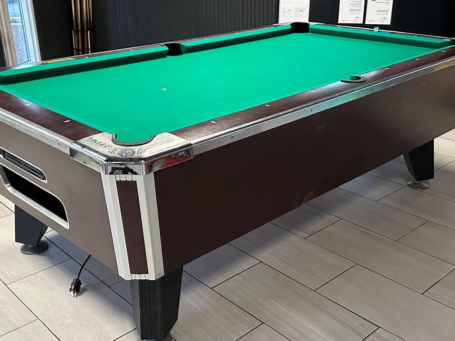 A pool table with a green felt surface, a brown frame, and a white border.