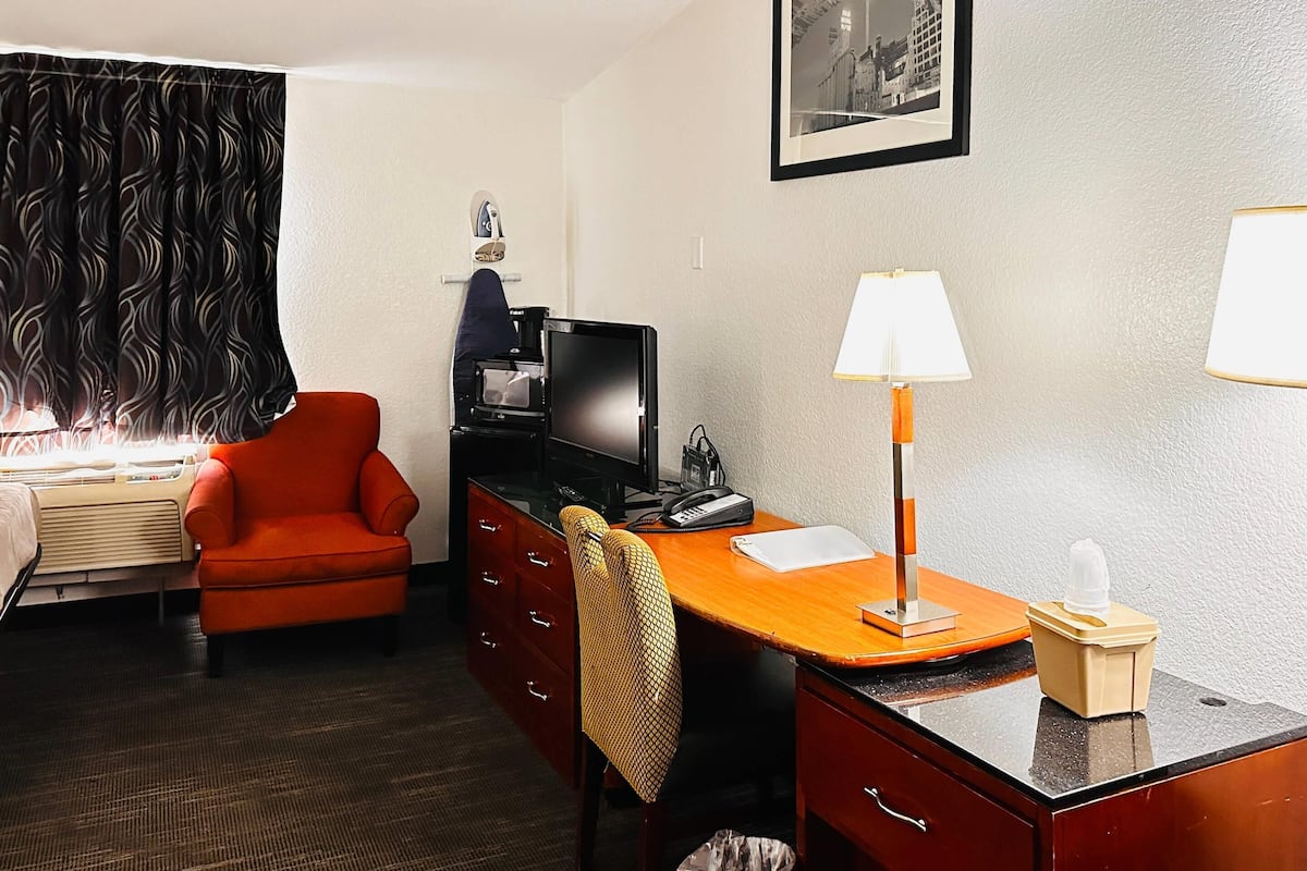 A hotel room with a bed, a desk with a lamp, a chair, a television, and a framed picture on the wall.
