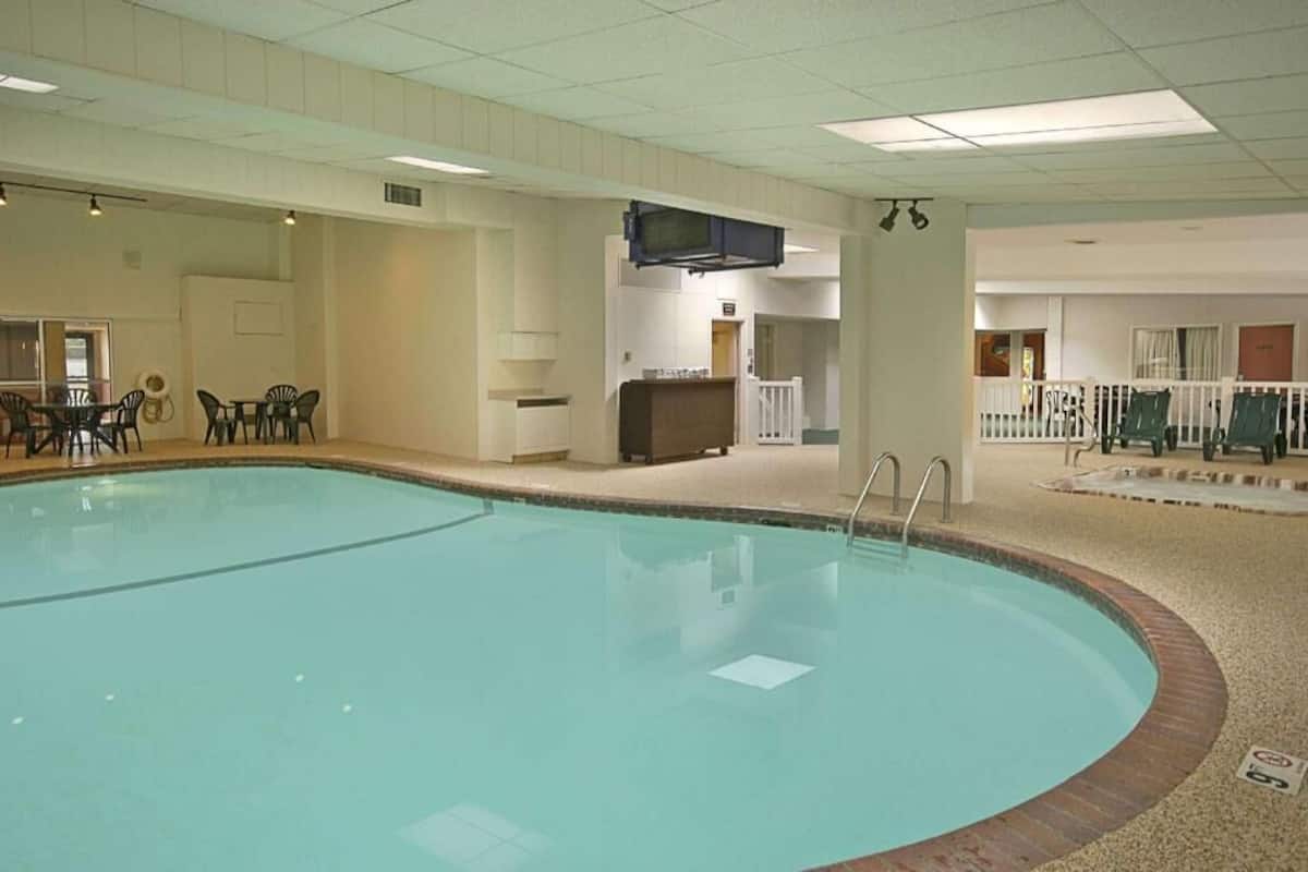 An indoor swimming pool with a tiled deck, a lounge area with chairs, and a small seating area with a table.