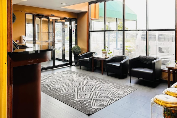 Zona de recepción con mostrador, asientos, alfombra estampada y ventanas amplias.