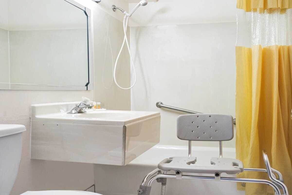 A bathroom with a sink, mirror, shower, and a wheelchair-accessible bench.