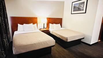 A hotel room with two beds, each with white linens and wooden headboards. There is a nightstand with a lamp between the beds.
