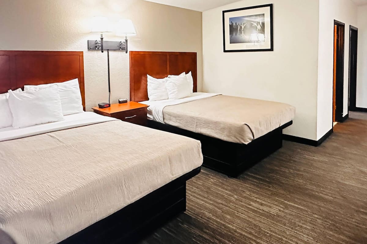 A hotel room with two beds, a nightstand with a lamp, a framed picture on the wall, and a wooden floor.
