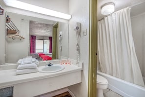 A bathroom with a white sink, a mirror, a hairdryer, a toilet, and a bathtub with a white curtain.