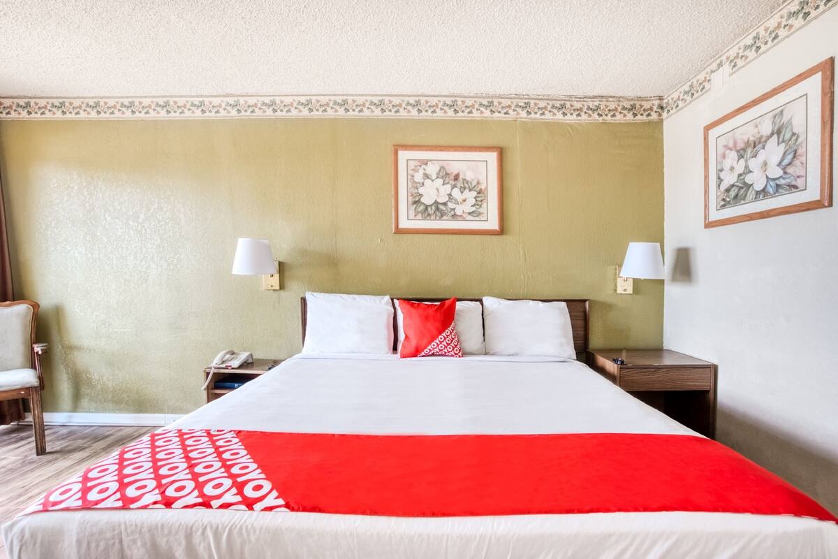 Ein Hotelzimmer mit einem großen Bett, zwei Nachttischen, einem Sessel und floralem Wandbild.