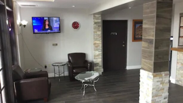 A modern living area with a sofa, a coffee table, a TV mounted on the wall, and a stone accent wall. - Extend-a-Suites Phoenix (Phoenix)