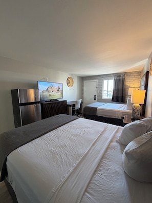 A hotel room with two beds, a desk, a television, and a refrigerator.