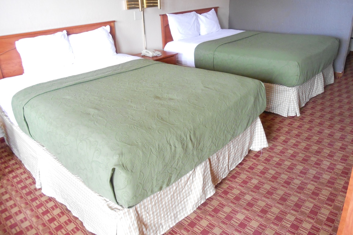 Habitación de hotel con dos camas, una mesita de noche, una lámpara y un cuadro colgado en la pared.