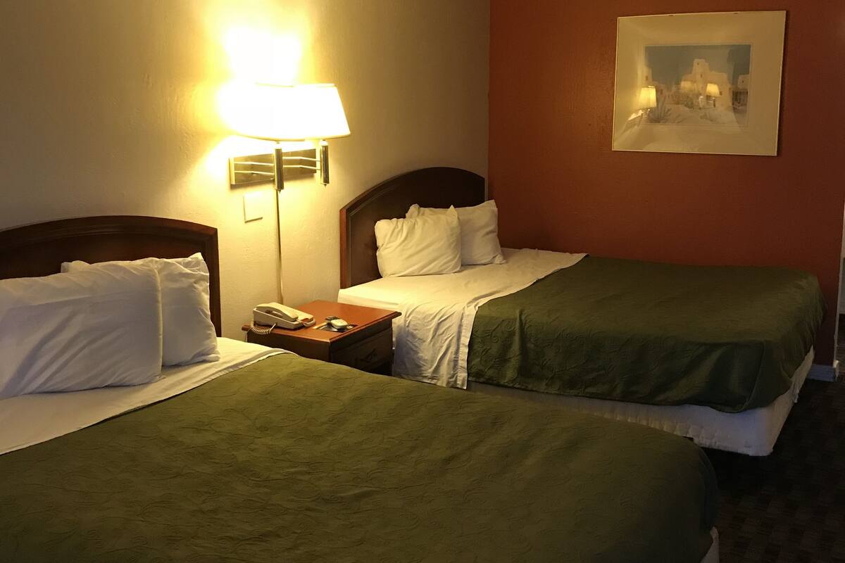 Ein Hotelzimmer mit zwei Betten, einem Nachttisch mit Lampe und einem gerahmten Bild an der Wand.