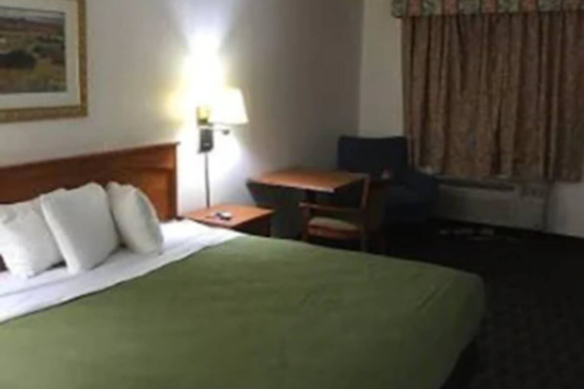 Ein Hotelzimmer mit Bett, Schreibtisch, Stuhl, Lampe und einem Fenster mit Vorhängen.