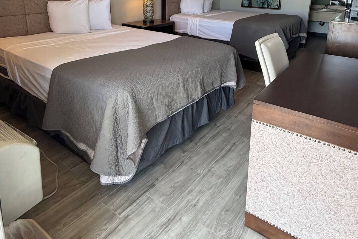 Ein Hotelzimmer mit zwei Betten, einem Schreibtisch, einem Sessel, einer Lampe und einem Bild an der Wand.