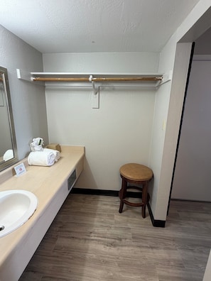 Un baño con lavamanos, espejo, toalla, taburete y un perchero para toallas.