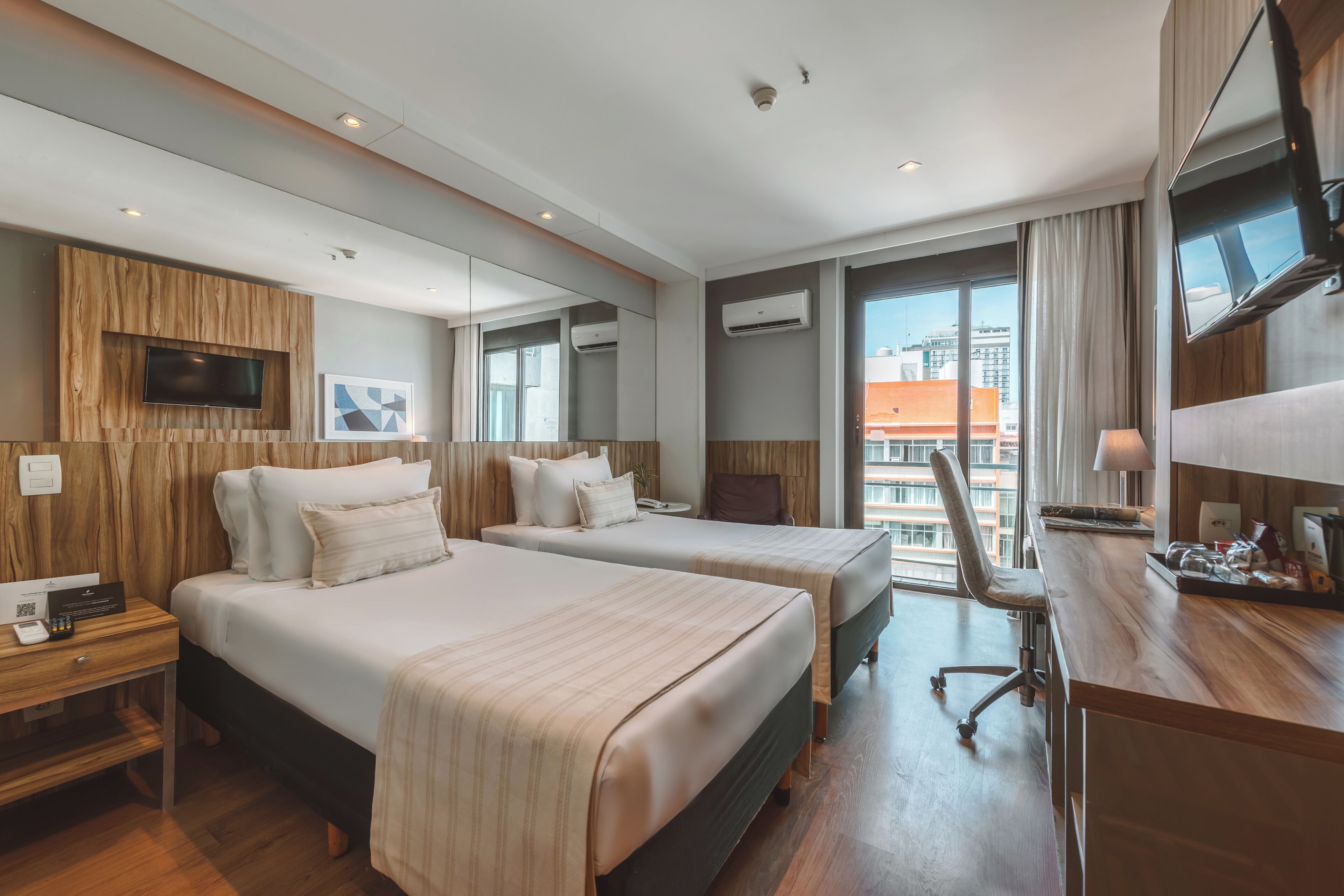 Une chambre d’hôtel avec deux lits, un bureau, une chaise, une télévision et une grande fenêtre.