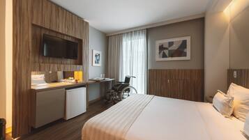 Habitación de hotel con cama, escritorio, silla, televisión y obras de arte en las paredes.