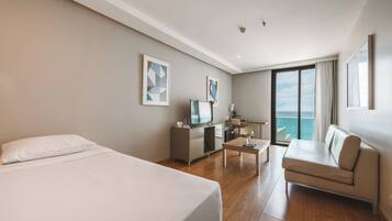 Quarto de hotel com cama, escrivaninha, sofá e uma janela grande com vista.