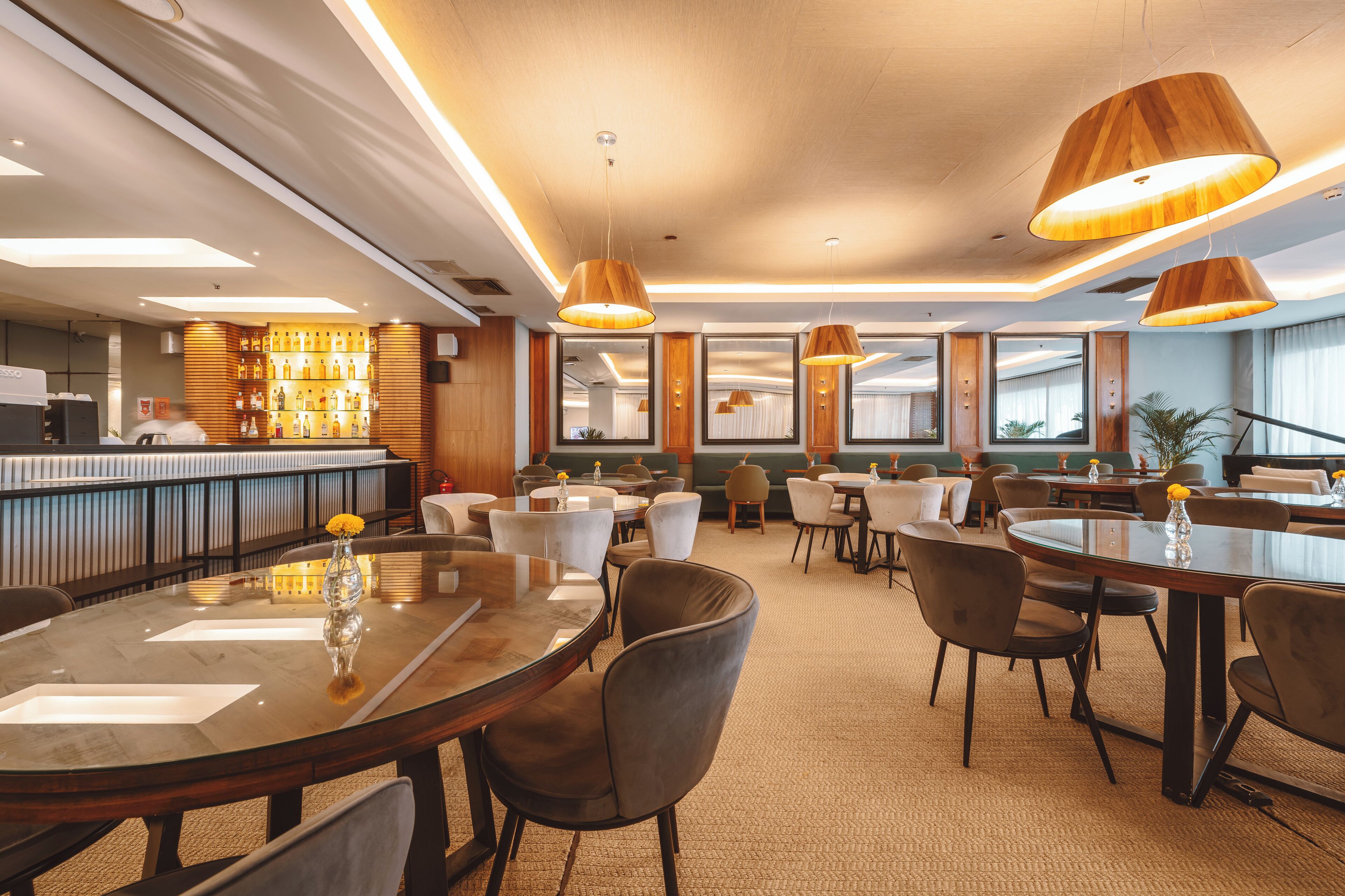 A modern hotel lobby with round tables, comfortable seating, a bar area, and large windows.