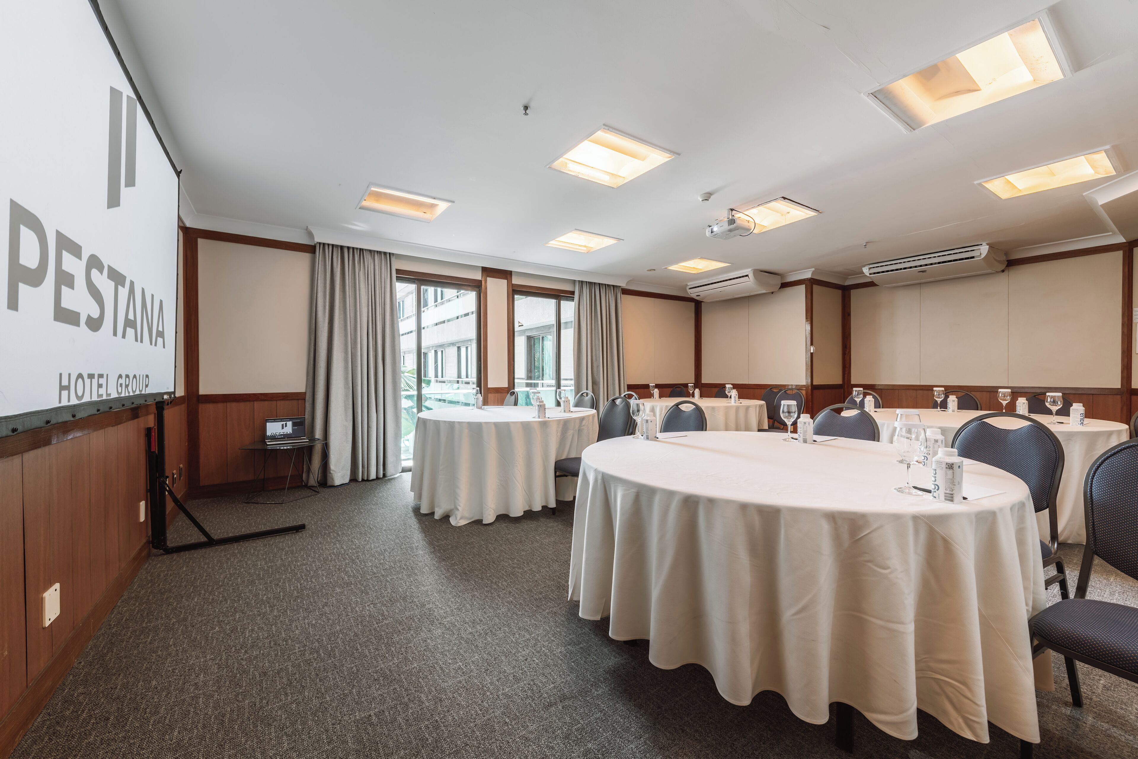 Ein Konferenzraum mit runden Tischen, Stühlen und einer Projektionsleinwand, die 'PESTANA HOTEL GROUP' zeigt.