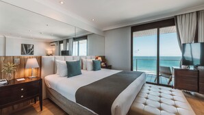 Habitación de hotel moderna con una cama grande, televisión, escritorio y balcón con vista al océano.