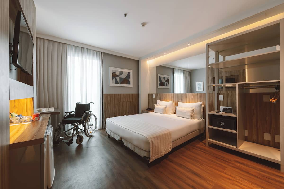 Une chambre d’hôtel équipée d’un lit, d’un fauteuil roulant, d’une table de chevet et d’une armoire intégrée.