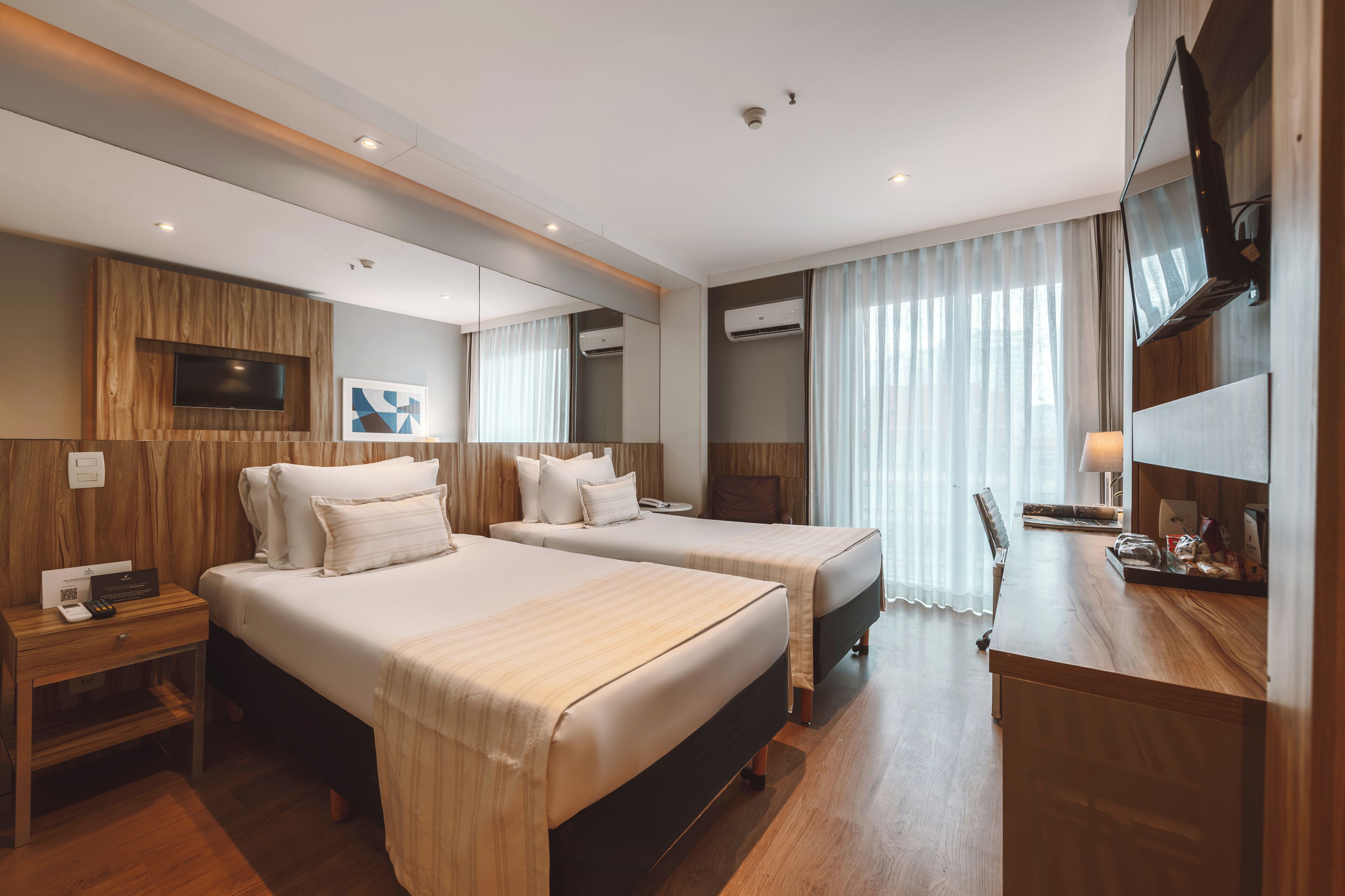 A hotel room with two beds, a desk, a TV, and a mirror.