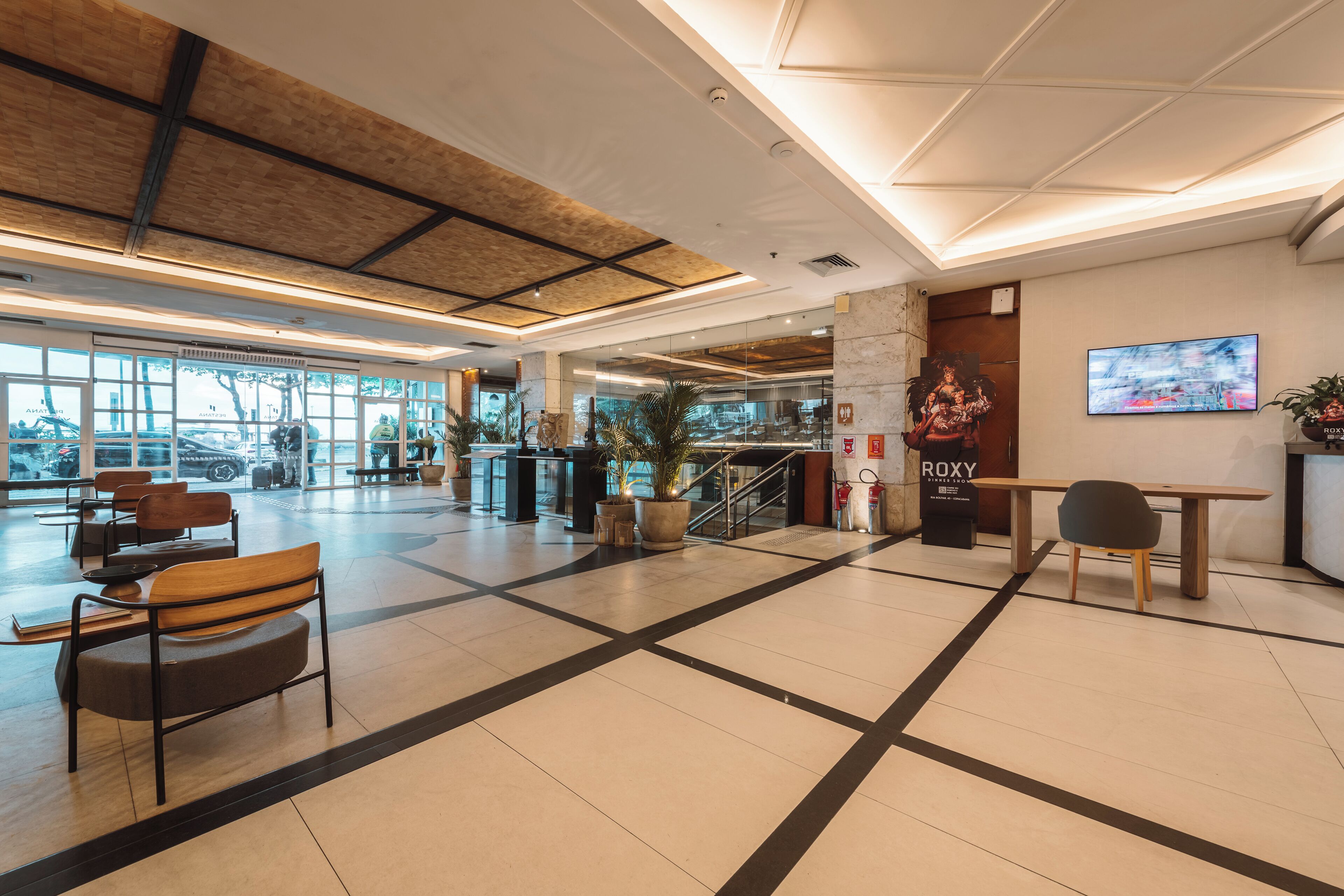 A spacious lobby with a high ceiling, a reception desk, seating areas, and large windows.