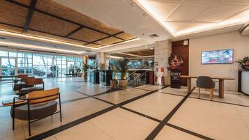 A spacious lobby with a high ceiling, a reception desk, seating areas, and large windows.