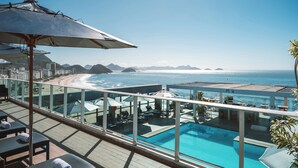 Piscina en la azotea con vista al océano y la playa, sillas de descanso y sombrillas.