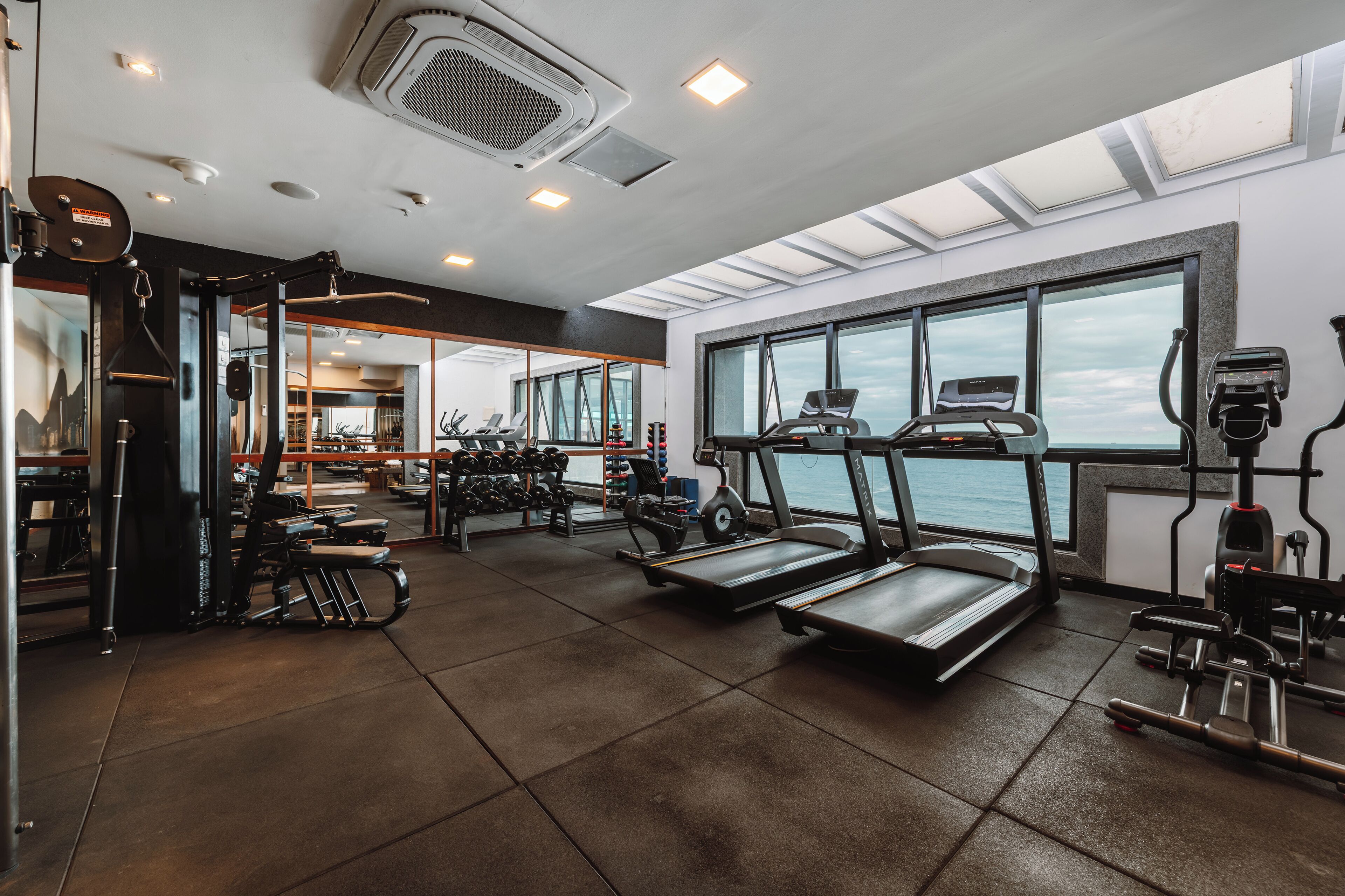 A gym with treadmills, weight machines, and a large window overlooking the sea.