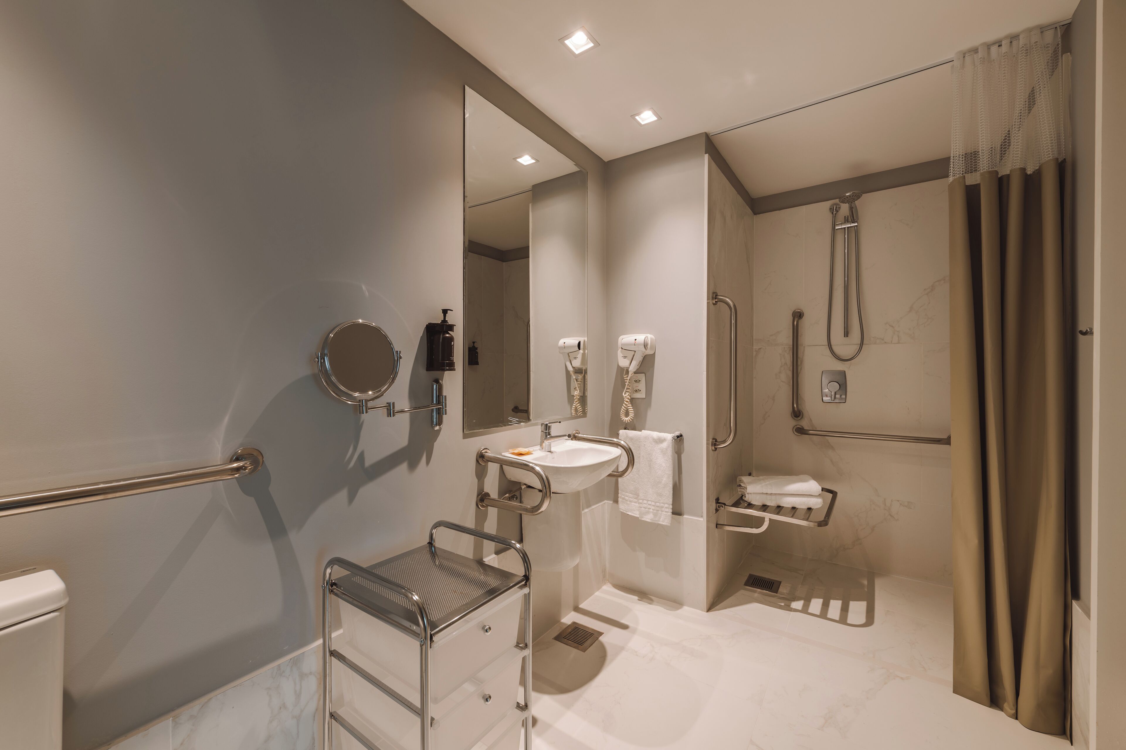 Un baño moderno con lavamanos, espejo, toallero, ducha y barras de apoyo.