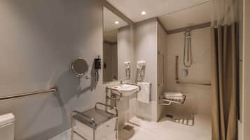 Un baño moderno con lavamanos, espejo, toallero, ducha y barras de apoyo.