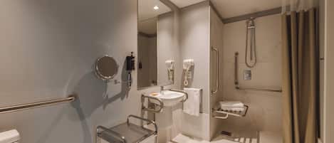 Un baño moderno con lavamanos, espejo, toallero, ducha y barras de apoyo.
