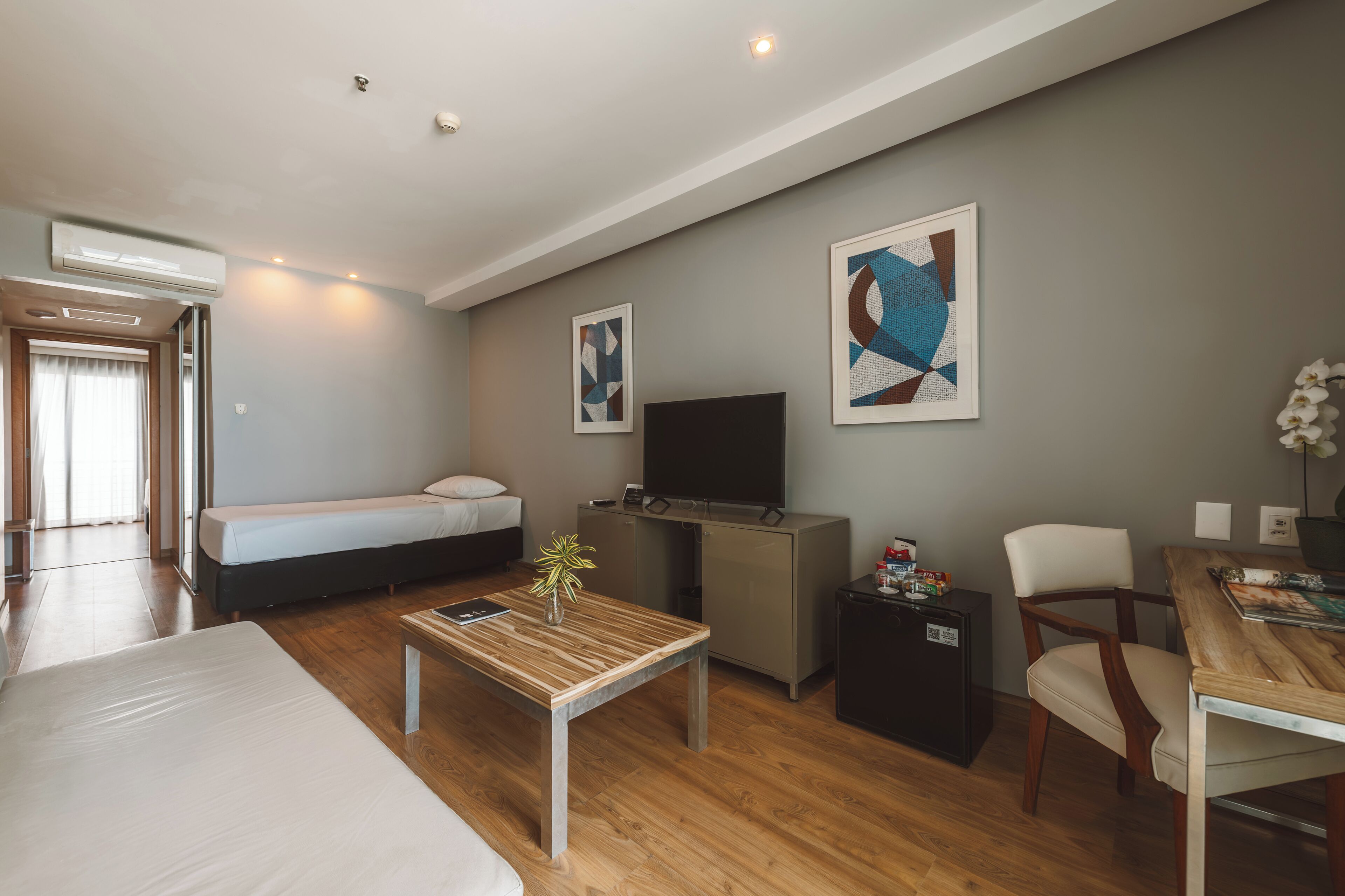 A modern hotel room with a bed, a sofa, a TV, a small table, and artwork on the walls.