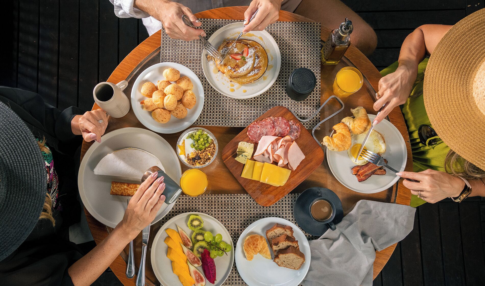 A group of people dining at an outdoor table with various breakfast items including eggs, pastries, and fruits.