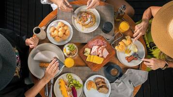 A group of people dining at an outdoor table with various breakfast items including eggs, pastries, and fruits.