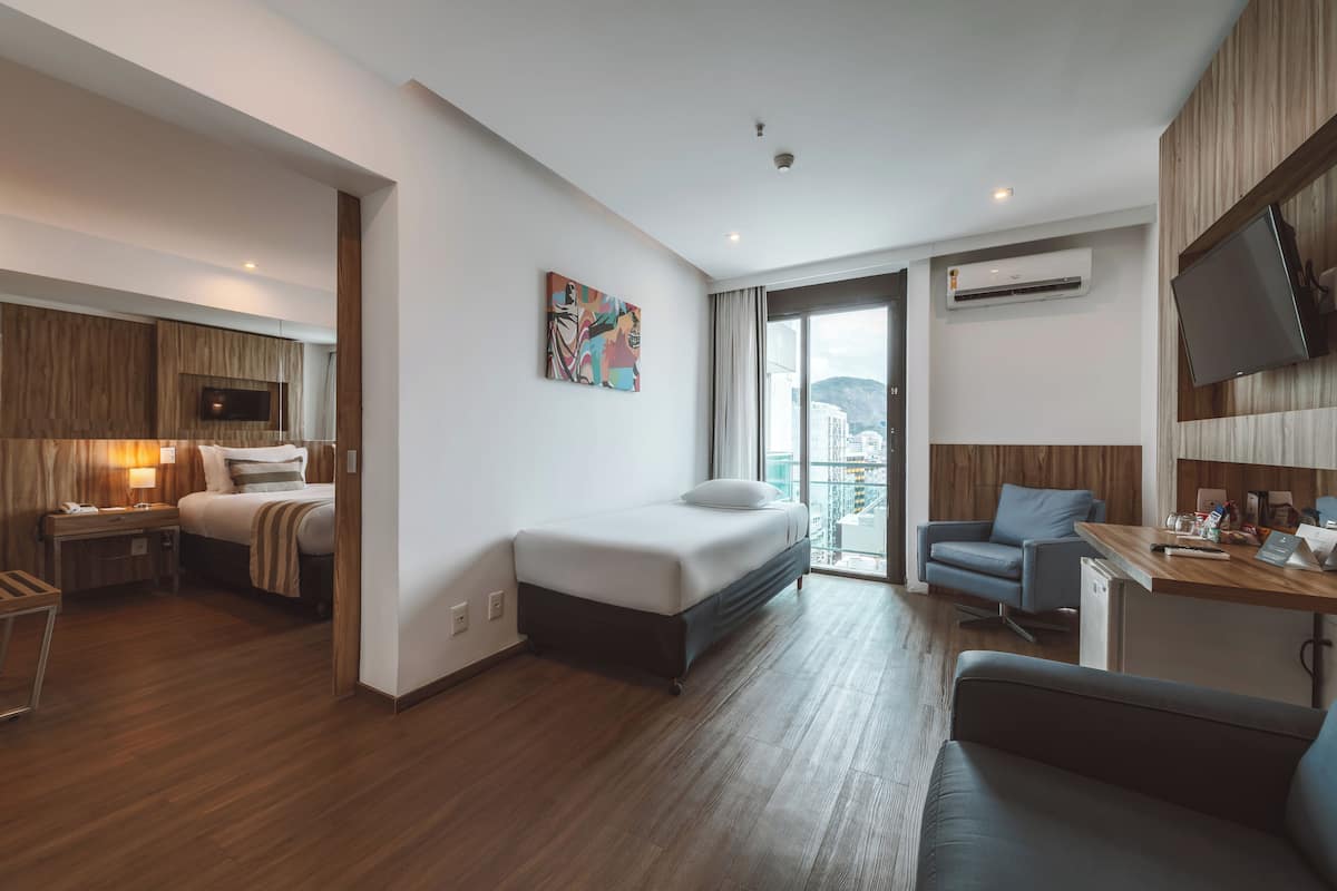 Une chambre d’hôtel moderne équipée d’un lit, d’un bureau, d’une chaise, d’une télévision et d’un balcon offrant une vue sur la ville.