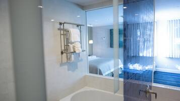 Un baño moderno con cabina de ducha de vidrio, bañera y puerta de vidrio que da a un dormitorio.