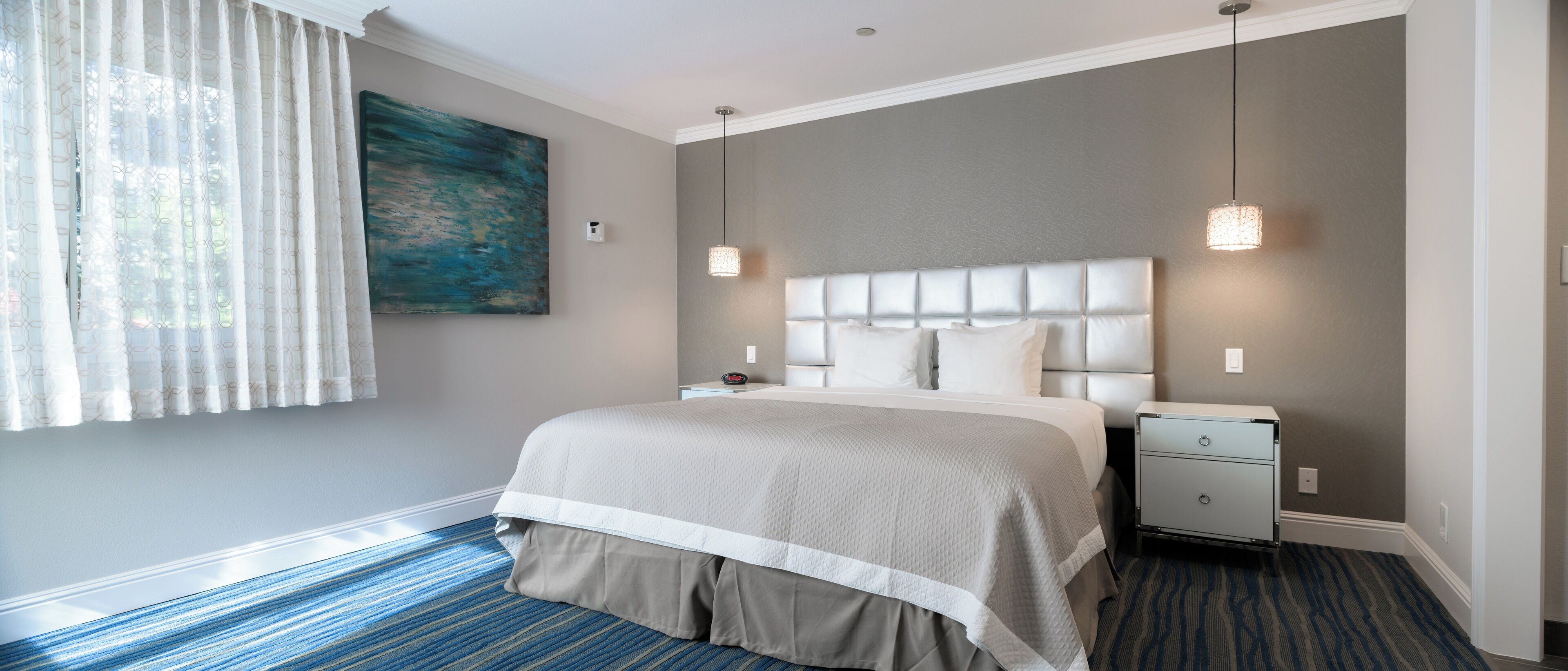 Une chambre d’hôtel bien rangée, avec un grand lit, une table de chevet et un tableau accroch é au mur.