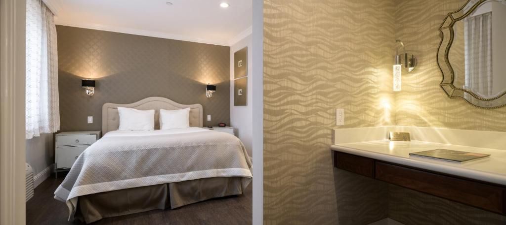 A hotel room with a bed, bedside lamps, a nightstand, and a bathroom with a mirror, sink, and towel rack.