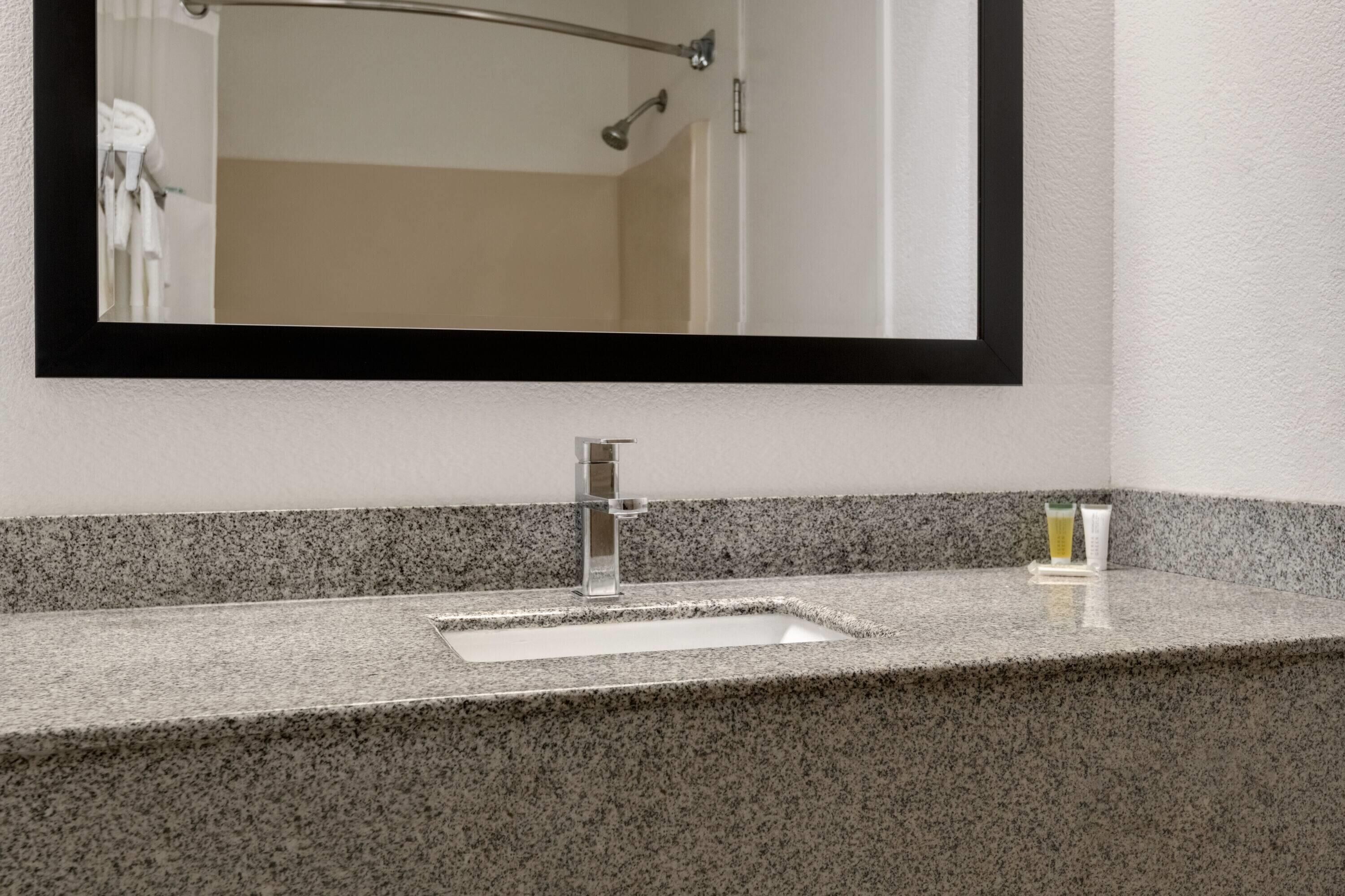 Un baño con encimera de granito, un lavabo y un espejo.