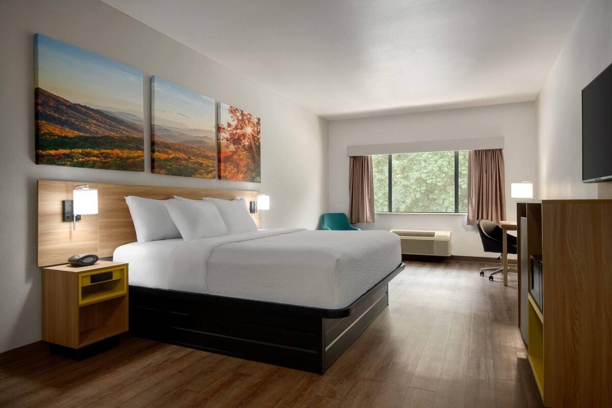 Una habitación de hotel moderna con una cama grande, mesitas de noche, un escritorio y un televisor.