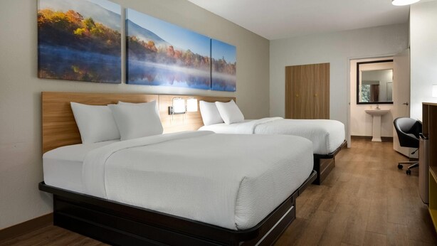 A hotel room with two beds, a wooden headboard, a desk with a chair, a mirror, and artwork on the wall. - Days Inn by Wyndham Lexington (Lexington)