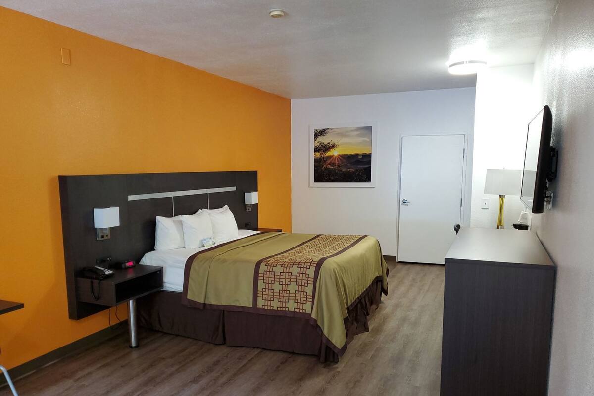 Una habitación de hotel con cama, mesita de noche, lámpara y un cuadro en la pared.