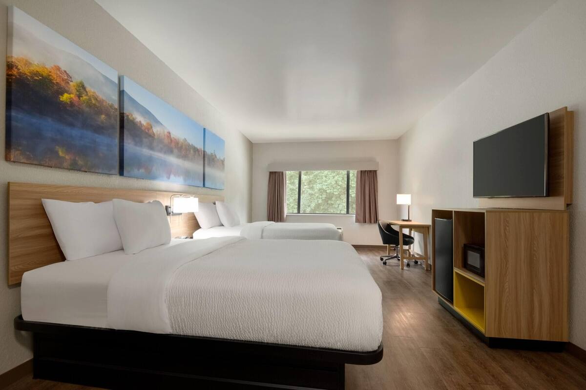 Una habitación de hotel con una cama grande, un escritorio, un televisor y obras de arte en la pared.
