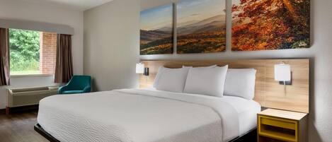 A hotel room with a large bed, a desk with a lamp, a chair, and a window with curtains.