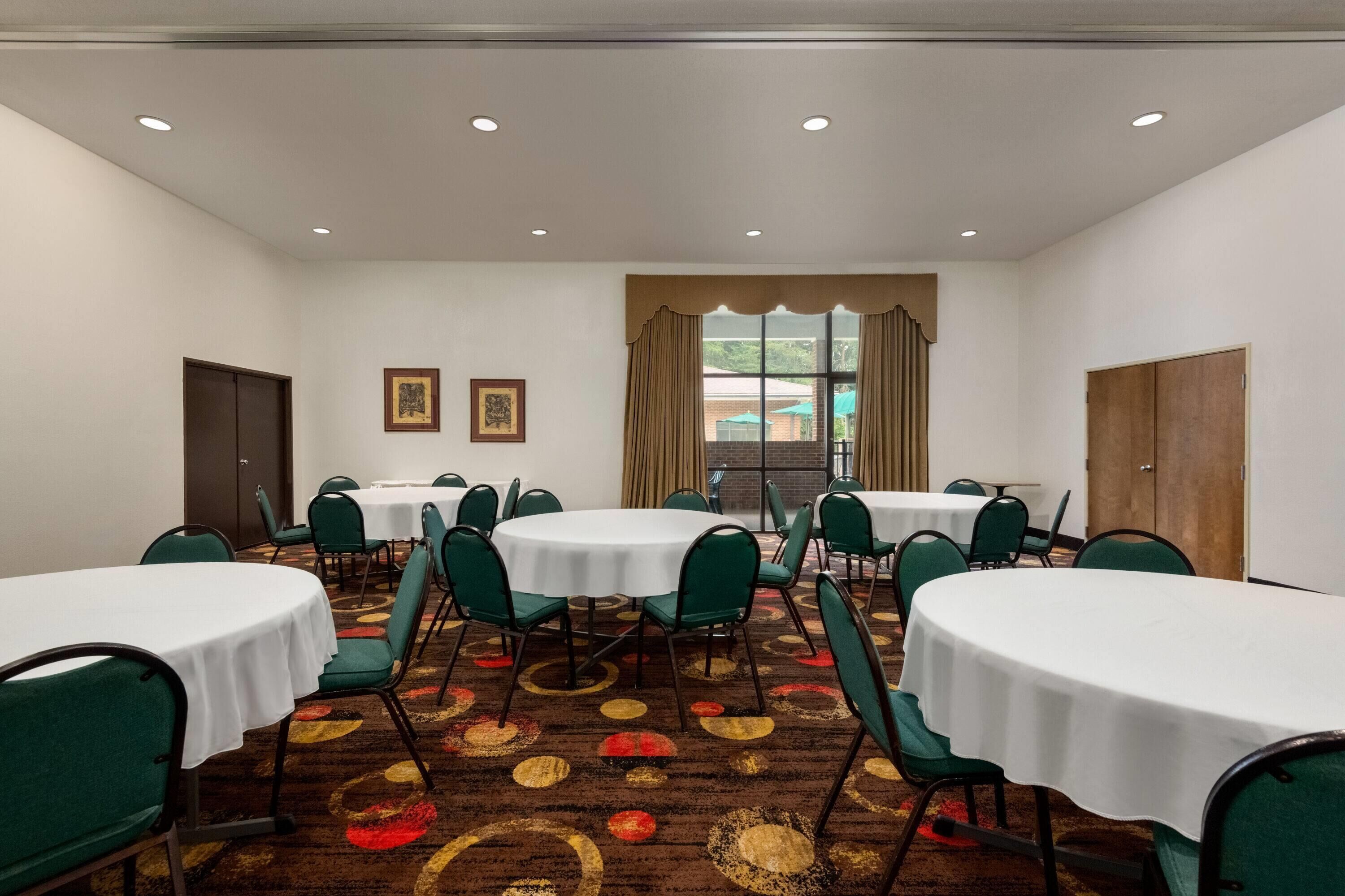 Un salón de conferencias con mesas redondas, sillas verdes y una alfombra estampada.