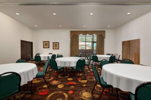Un salón de conferencias con mesas redondas, sillas verdes y una alfombra estampada.