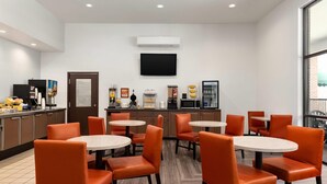 A modern dining area with orange chairs and round tables, a coffee machine, and a flat-screen TV mounted on the wall. - Days Inn by Wyndham Lexington (Lexington)
