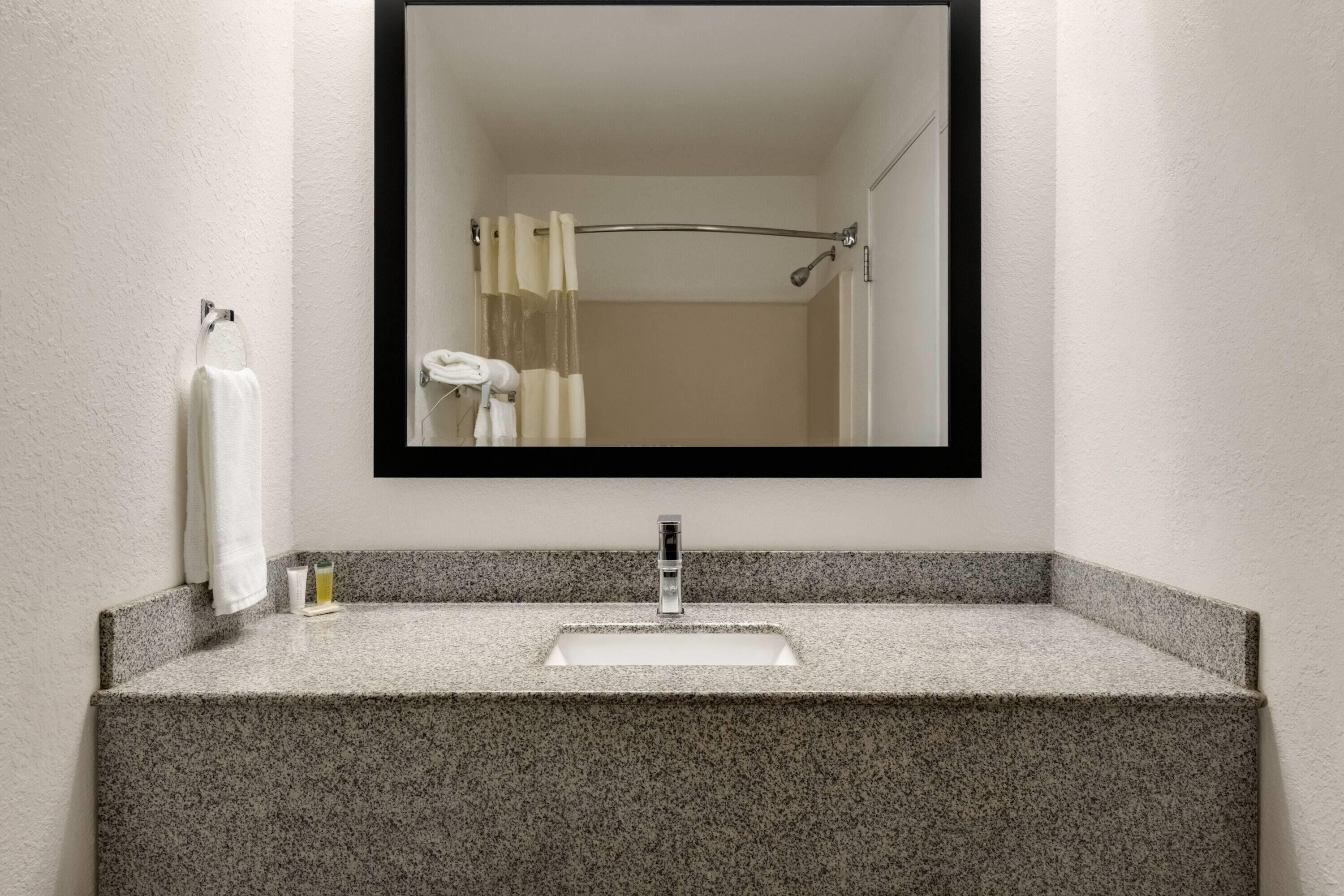 A bathroom with a granite countertop sink, a mirror, and a towel rack.